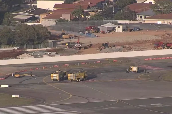 Imagem aérea colorida mostra pista de aeroporto com cerca de três veículos e é possível ver um pequeno ponto branco no meio da pista - Metrópoles