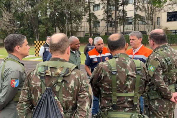 Imagem mostra militares ao lado de homens com trajes da defesa civil - Metrópoles