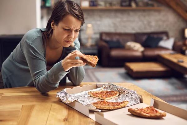 Mulher com expressão triste comendo pizza - Metrópoles