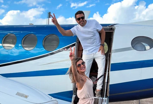 Casal na porta de helicóptero, sorrindo e acenando com os braços