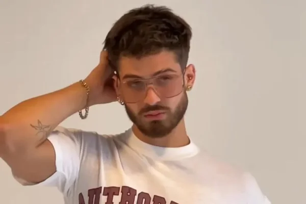 Foto do ator João Guilherme. Ele usa blusa branca, pulseira, óculos e está fazendo pose para foto - Metrópoles