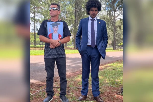 Pai de militar da FAB morto dentro de anexo do Ministério da Defesa ao lado do advogado do caso. Ele segura, à esquerda, uma foto do filho abraçada a si e o advogado, um homem negro de terno, olha para a câmera - Metrópoles