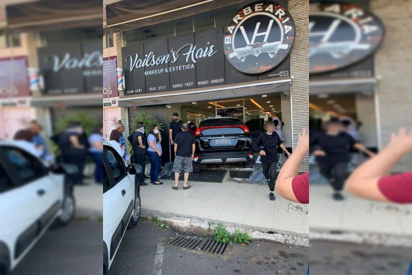 Carro preto entra em fachada de vidro de barbearia. Várias pessoas na frente do local