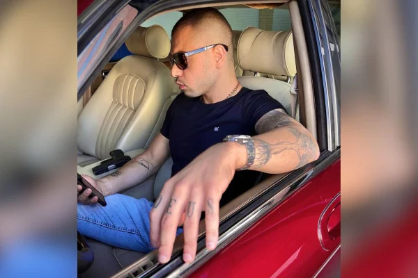 Foto de homem em carro mexendo no celular com arma ao lado