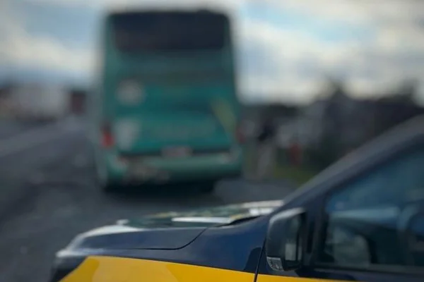 Imagens coloridas mostram parte do capô de uma viatura da PRF, cores amarela e azul, e traseira de ônibus em imagem desfocada, ao fundo