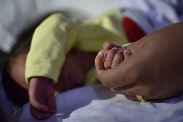 mãe segura mão de bebê com roupinha amarela - Metrópoles
