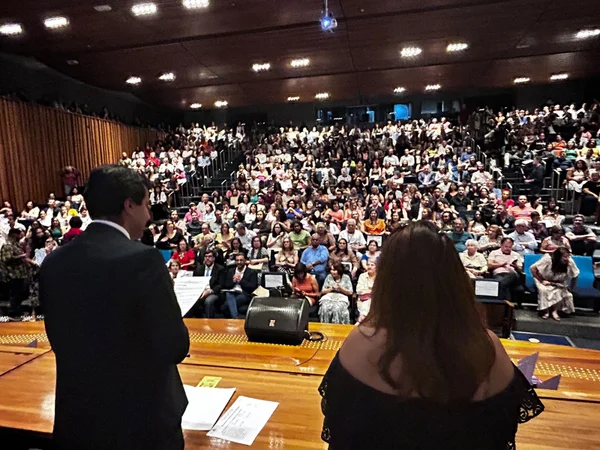 Imagem colorida de pessoas sentadas em um auditório - Metrópoles