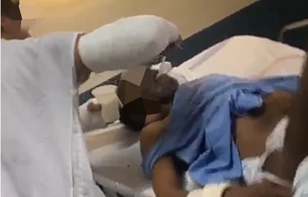 Em foto colorida homem com braço engessado dá colida na boda de senhor amarrado em cama de hospital - Metrópoles