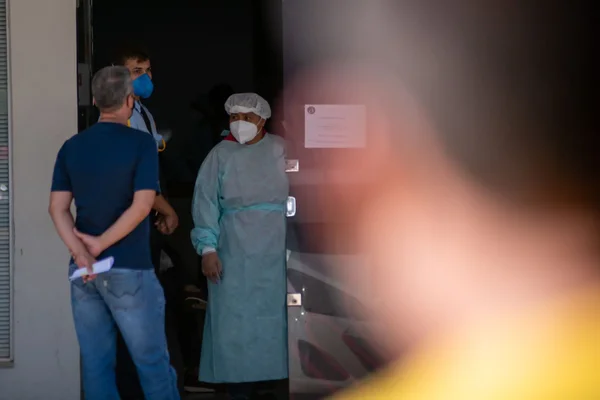 mulher com materiais de proteção - touca, roupa de proteção e máscara, conversando com dois homens em uma porta