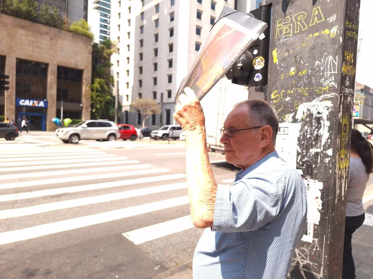 Pedestre se protege do sol com jornal em trecho da Avenida Paulista, em São Paulo