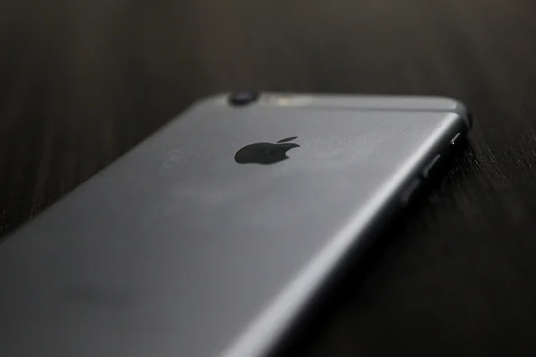 Imagem de um aparelho celular iPhone da primeira geração, de 2007, da Apple. O aparelho é branco e está sobre uma mesa preta.