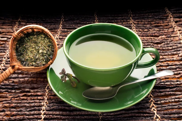 Foto colorida de xícara verde com chá e ervas ao lado - Nutricionista lista os 3 melhores chás para quem tem gordura no fígado - Metrópoles