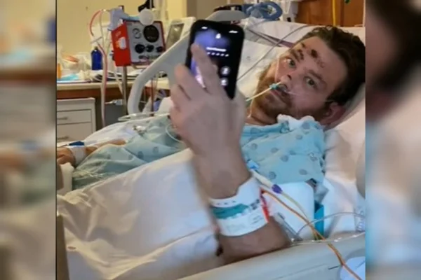 um homem internado deitado em uma maca com uma celular na mão