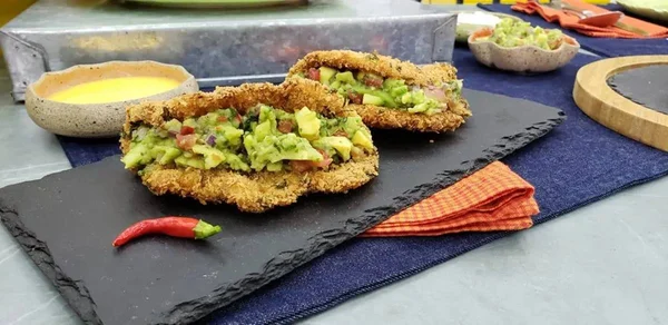 Receita de tortilha de frago feita no progrma Mais Você, da Globo. Na foto, duas delas aparecem sob tábua de pedra escura, com recheio variado, molho e pimenta ao lado - Metrópoles