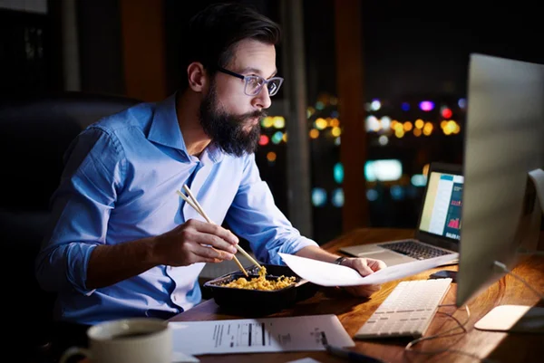 Homem come em frente ao computador