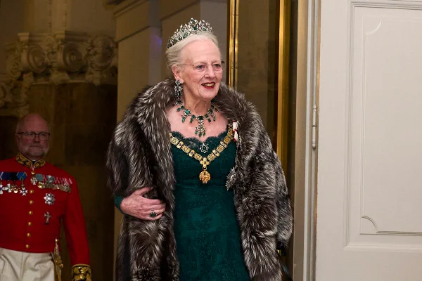 Foto colorida de mulher com coroa, joias e um vestido verde-esmeralda. Ela usa uma capa - Metrópoles