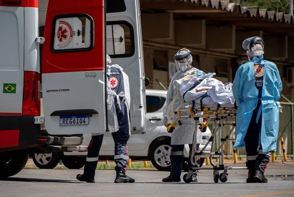 Profissionais da saúde colocam maca com paciente em ambulância