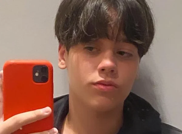 Em foto colorida jovem tira selfie com celular de capa laranja - Metrópoles