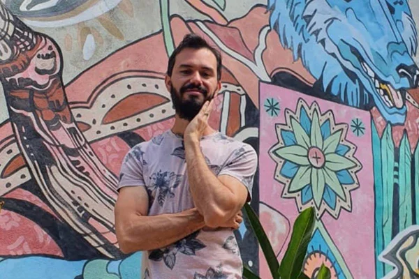 Chef Lui Veronese sorri com mão no rosto em frente a uma parede colorida com desenhos