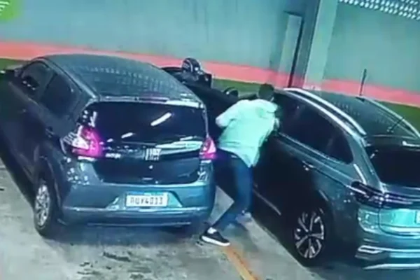 Imagem colorida de homens armados abordando mulher dentro de carro e um estacionamento. Metrópoles