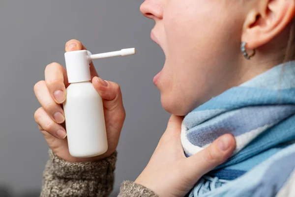 Foto colorida de mulher aplicando spray na garganta - Metrópoles