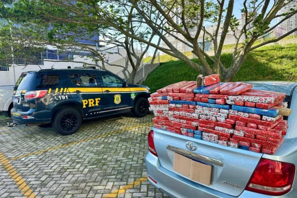 Foto colorida de viatura da PRF ao lado de carro no qual foram apreendidos mais de 130 kgs de maconha embrulhados como presente de natal