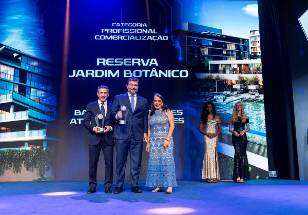 Fotografia colorida mostrando três pessoas, dois homens e uma mulher, recebendo troféu em premiação-Metrópoles