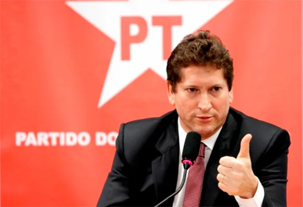 Jilmar Tatto, um dos dirigentes da campanha à presidência de Lula, discursa com a mão fazendo sinal de "joia" diante de microfone e com painel do PT ao fundo - Metrópoles