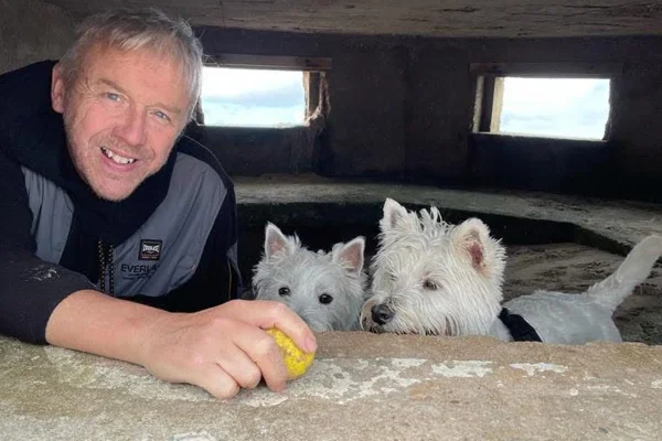 Foto colorida de homem sorrindo e dois cachorros. -Metrópoles