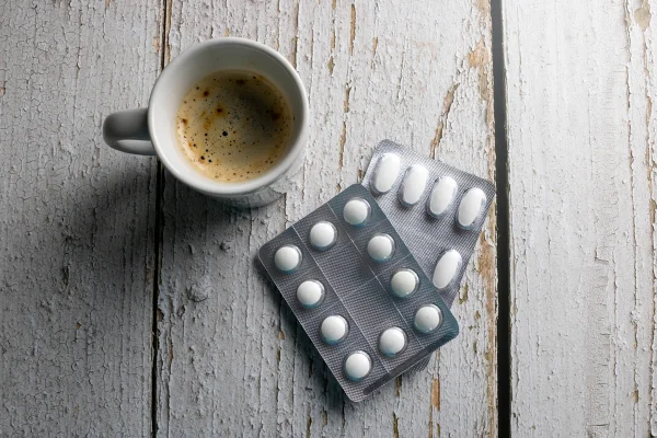 Foto colorida de xícara de café e cartelas de medicamentos - Metrópoles