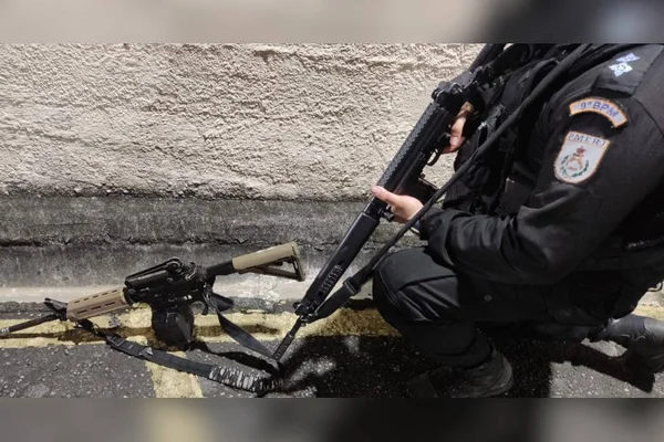 polical segura arma em frente a fuzil no chão