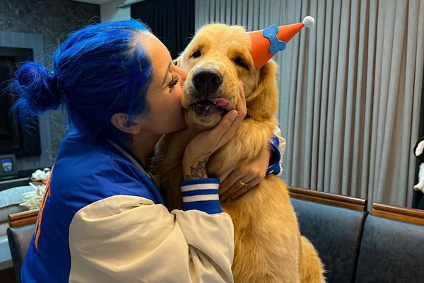 Imagem de Maggie e Ianka. A influencer tem o cabelo azul e usa um casaco azul e branco. O cachorro é da raça Golden Retriever - Metrópoles