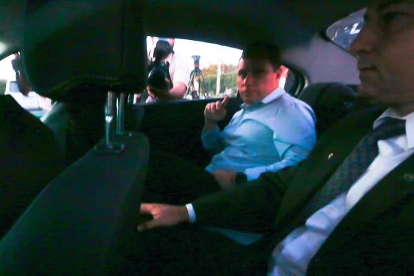 Foto colorida de Mauro Cid sentado no banco de trás de carro saindo da PF - Metrópoles