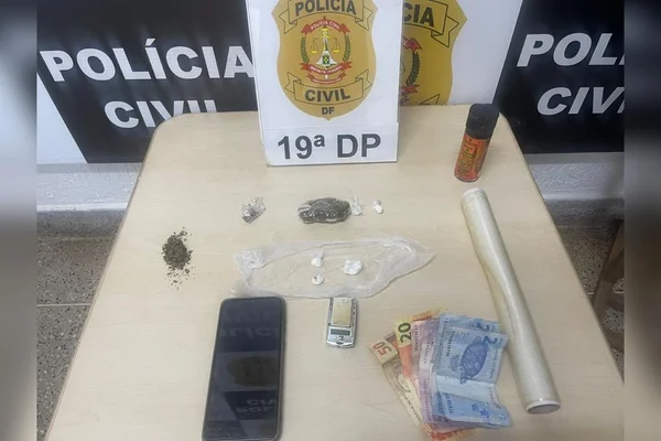 Celular preto, dinheiro e porções de entorpecentes em cima de uma mesa branca - Metrópoles