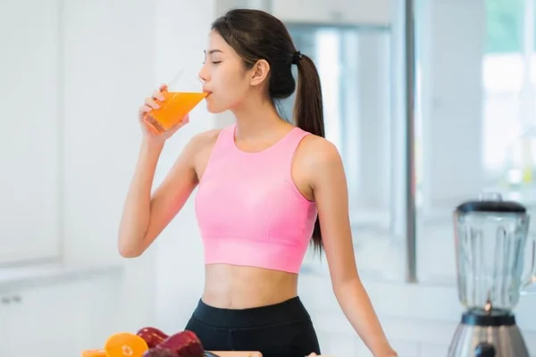 Mulher de blusa rosa tomando um suco sentada na cozinha - Metrópoles