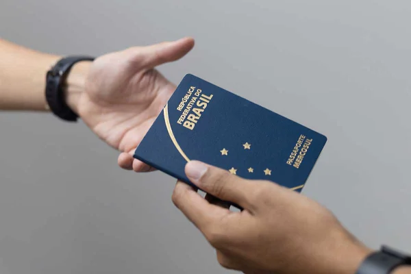 Imagem colorida: mãos de duas pessoas seguram passaporte Brasileiro PF - Metrópoles