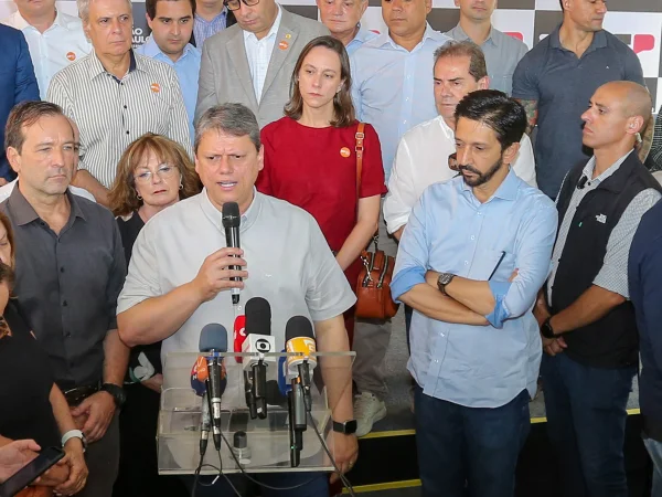 Imagem colorida mostra Tarcísio de Freitas, cercado de pessoas, falando ao microfone