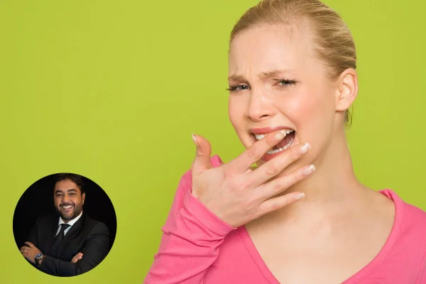 Mulher branca e loira está com o dedo nos dentes d a frente simbolizando dor e sensibilidade. No lado inferior esquerdo, há um circulo com a foto do dentista