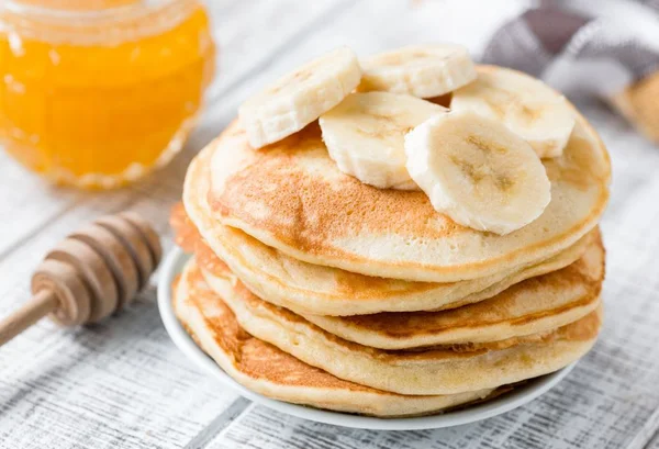 Panqueca de banana com algumas bananas picadas em cima com um mel ao lado em um pote de vidro - Metrópoles