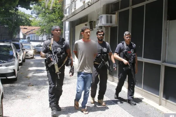 Imagem colorida de homem sendo conduzido por policiais - Metrópoles