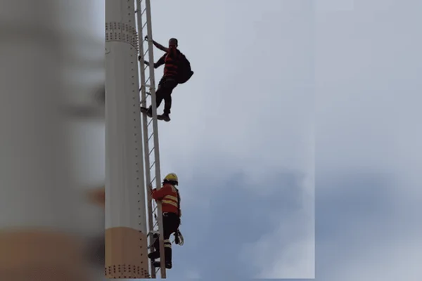Homem de camisa preta e vermelha com mochila nas costas descendo escadas enquanto bombeiro acompanha