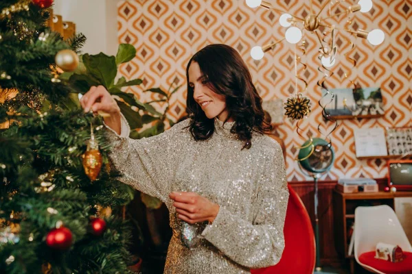 Mulher jovem segurando bola de Natal ao lado de árvore natalina - Metrópoles