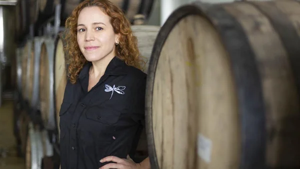 Na imagem, uma mulher branca e ruiva posa em frente a barris de cerveja