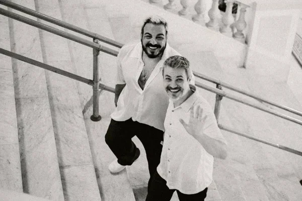 foto em preto e branco de escada na qual sobem dois homens de mãos dadas e sorrindo - metrópoles