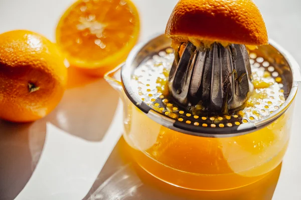 Imagem mostra um espremedor de laranja cheio, e vários pedaços da fruta - Metrópoles
