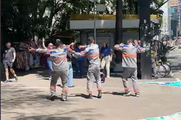 imagem de baixa qualidade mostra homens com roupa da Enel dançando na calçada de uma avenida