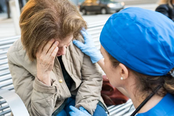 Médica ajudando uma mulher idosa na rua. Dor de cabeça, exaqueca, AVC, derrame