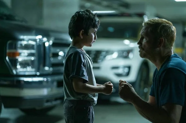 foto colorida de homem conversando com menino em estacionamento com carros ao fundo - metrópoles