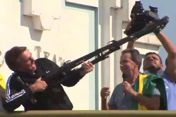 ex-presidente jair bolsonaro usa casaco preto e segura arma de fogo apontada para cima - Metrópoles