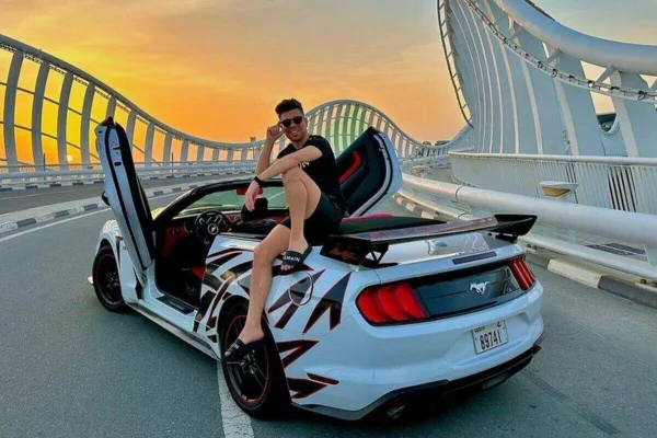 Foto colorida de homem sentado sobre carro de luxo estacionado em ponte - Metrópoles